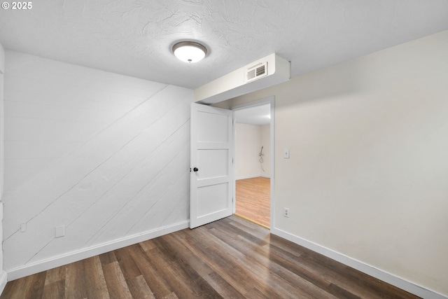 unfurnished room featuring dark wood-style floors, a textured ceiling, visible vents, and baseboards