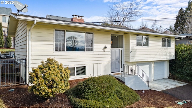 bi-level home with a garage, driveway, a chimney, and fence