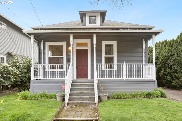 bungalow-style house with a shingled roof, a front lawn, and covered porch