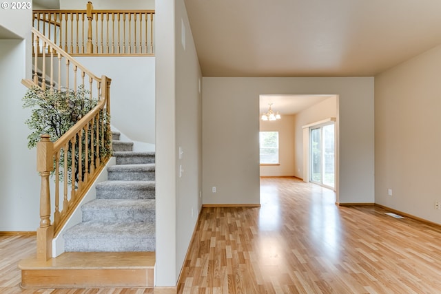 stairs with wood-type flooring and an inviting chandelier