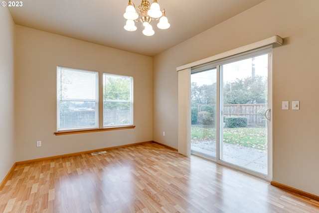 empty room with light hardwood / wood-style floors, a healthy amount of sunlight, and an inviting chandelier