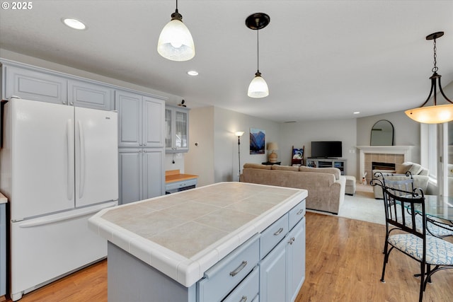 kitchen featuring freestanding refrigerator, tile counters, a center island, and light wood finished floors