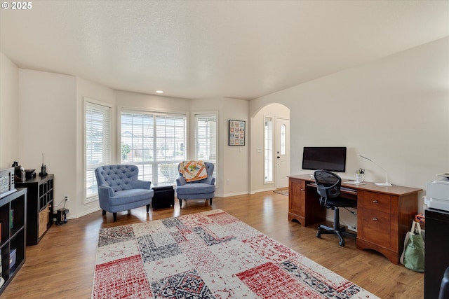 office with baseboards, light wood-type flooring, and arched walkways