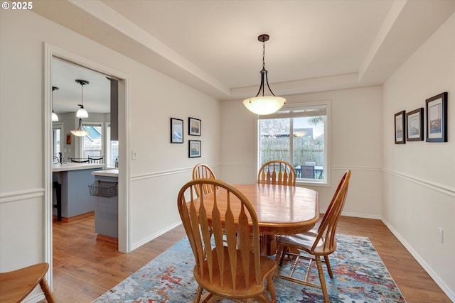 dining room with a raised ceiling, baseboards, and light wood-style flooring