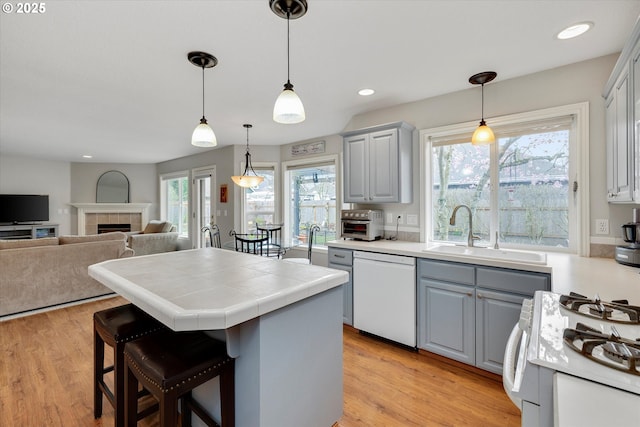 kitchen featuring light wood-type flooring, white appliances, gray cabinetry, a kitchen island, and a sink