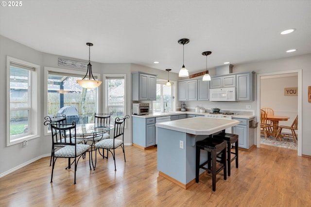 kitchen with gray cabinets, light wood-type flooring, white microwave, and a kitchen island