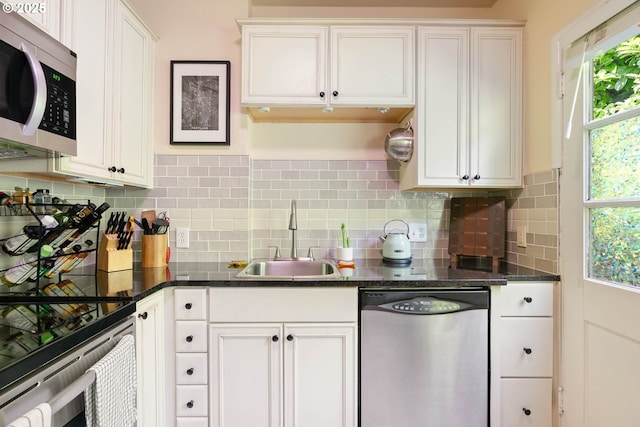 kitchen with appliances with stainless steel finishes, a sink, plenty of natural light, and white cabinetry