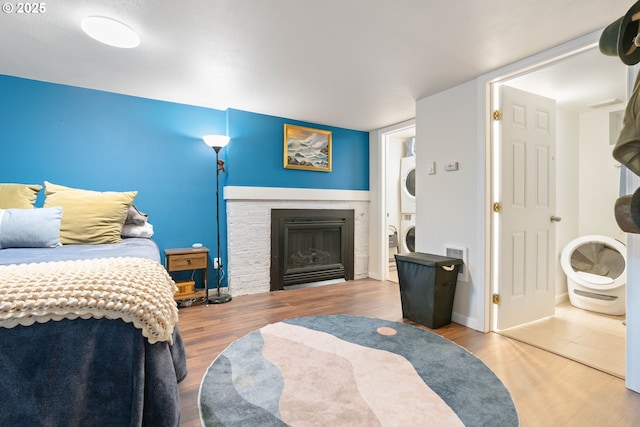 bedroom featuring stacked washer / dryer, wood finished floors, and a fireplace