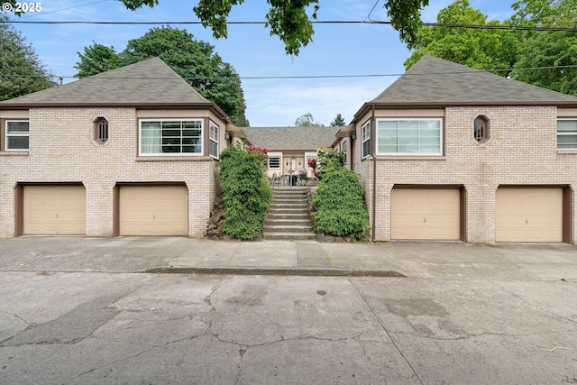 view of front of house with roof with shingles, brick siding, a garage, and driveway