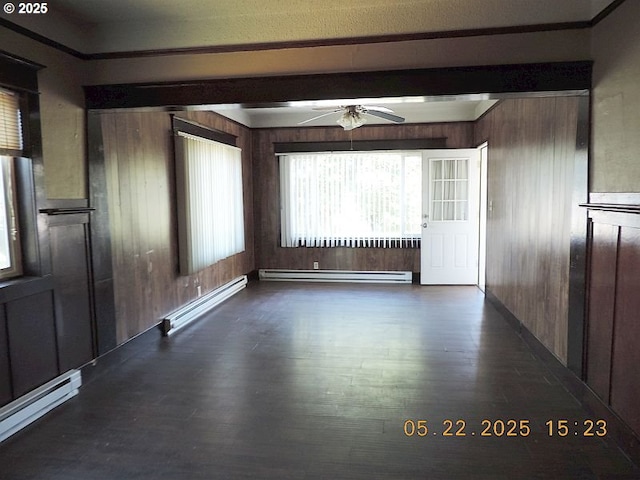 911 F St, The Dalles, OR 97058 - empty room featuring a baseboard heating unit, a ceiling fan, dark wood-style floors, wooden walls, and a baseboard radiator