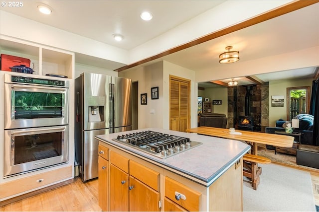 3820 Kenthorpe Way W, Linn, OR 97068 - kitchen with appliances with stainless steel finishes, light wood-style flooring, open floor plan, a center island, and a wood stove