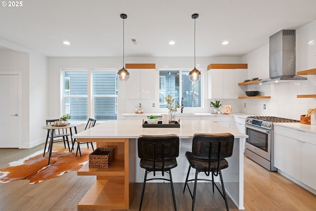 kitchen with stainless steel range with gas stovetop, wall chimney exhaust hood, modern cabinets, open shelves, and white cabinetry