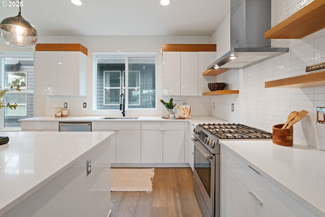 kitchen featuring wall chimney range hood, white cabinetry, open shelves, appliances with stainless steel finishes, and a sink