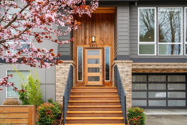 view of exterior entry featuring brick siding, an attached garage, and driveway