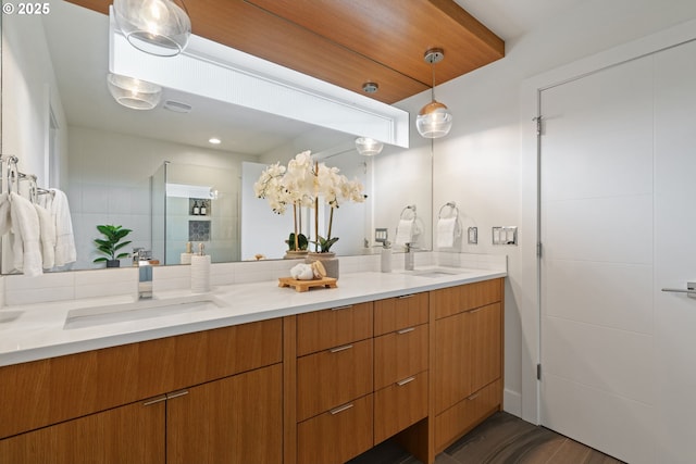 bathroom featuring a sink, a tile shower, double vanity, and wood finished floors