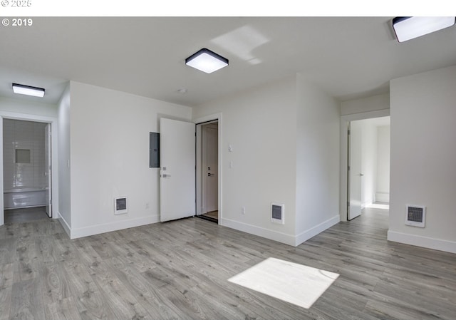 spare room with light wood-type flooring, electric panel, baseboards, and visible vents