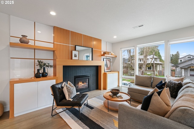 living room featuring a tiled fireplace, visible vents, recessed lighting, and light wood-style floors