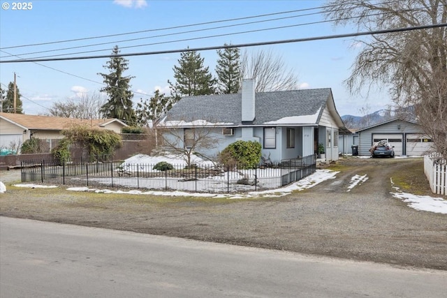 view of front facade with a garage, driveway, a fenced front yard, a chimney, and an outbuilding