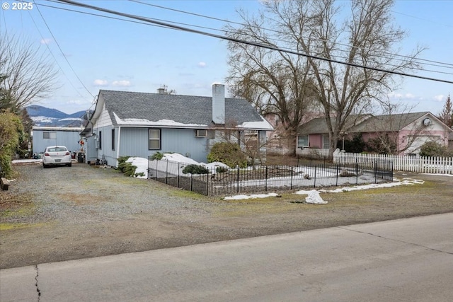 view of front of house with a fenced front yard, roof with shingles, a chimney, a mountain view, and driveway