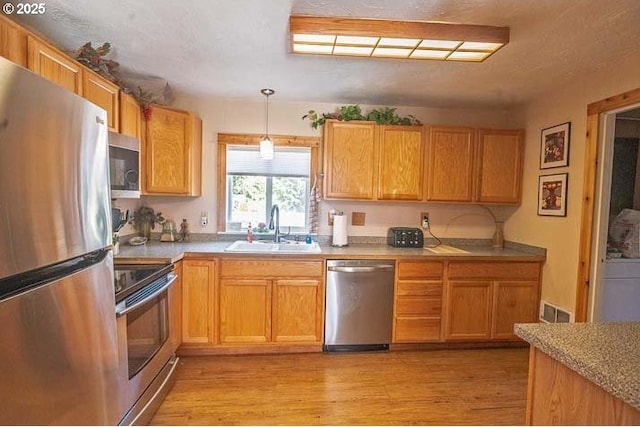 kitchen with pendant lighting, appliances with stainless steel finishes, a sink, light countertops, and light wood-style floors