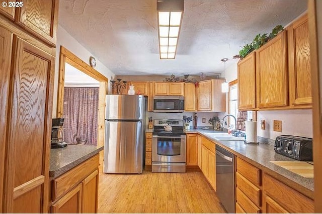 kitchen featuring a sink, light wood finished floors, stainless steel appliances, a toaster, and pendant lighting