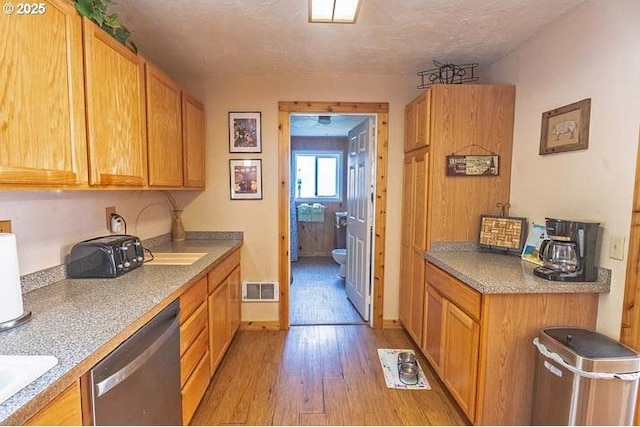 kitchen with visible vents, brown cabinetry, light wood-style floors, a sink, and dishwasher