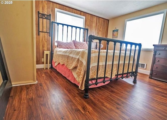 bedroom with wooden walls, baseboards, visible vents, and wood finished floors