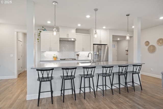 kitchen featuring decorative backsplash, a sink, baseboards, under cabinet range hood, and stainless steel appliances