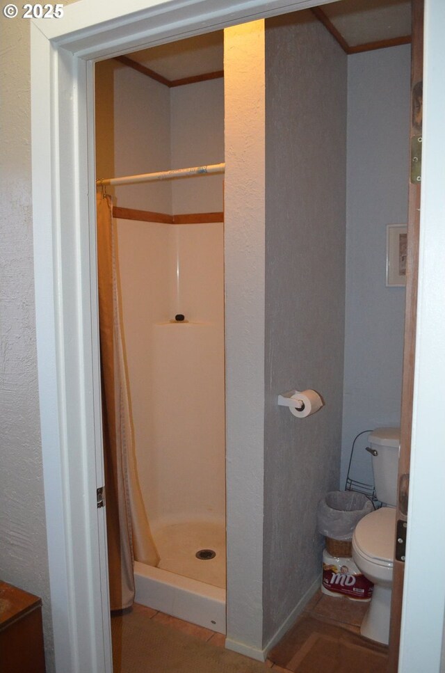 full bathroom featuring a stall shower, toilet, and a textured wall