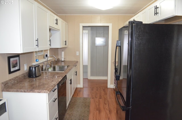 kitchen featuring black appliances, a sink, wood finished floors, white cabinets, and baseboards