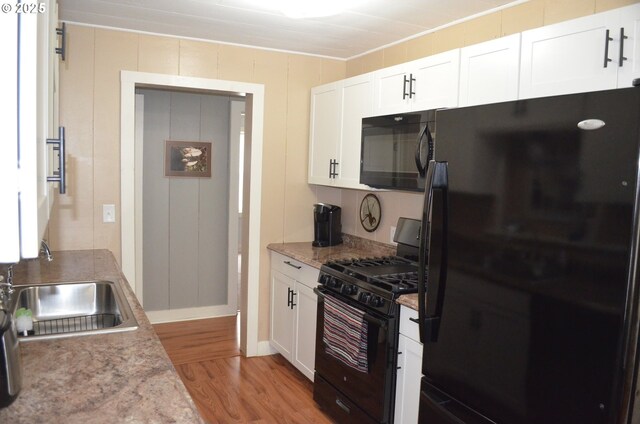 kitchen featuring black appliances, a sink, light wood-style flooring, white cabinets, and ornamental molding