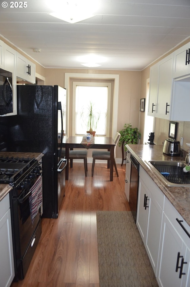 kitchen with black appliances, a sink, wood-type flooring, and white cabinetry