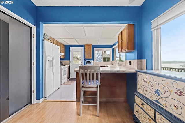 404 Chinook Ave, Astoria, OR 97103 - kitchen with white appliances, light wood finished floors, brown cabinetry, a sink, and a peninsula