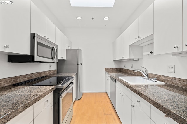 kitchen with a sink, stainless steel appliances, white cabinets, light wood-style floors, and dark countertops