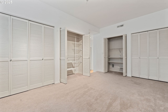 unfurnished bedroom featuring carpet, visible vents, and two closets