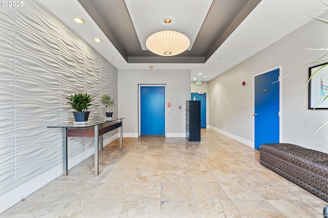 interior space featuring elevator, a raised ceiling, baseboards, and an accent wall