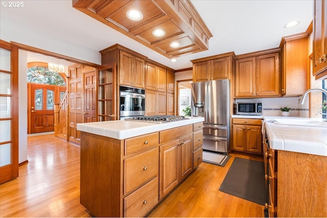 kitchen with appliances with stainless steel finishes, sink, a center island, tile counters, and light hardwood / wood-style floors