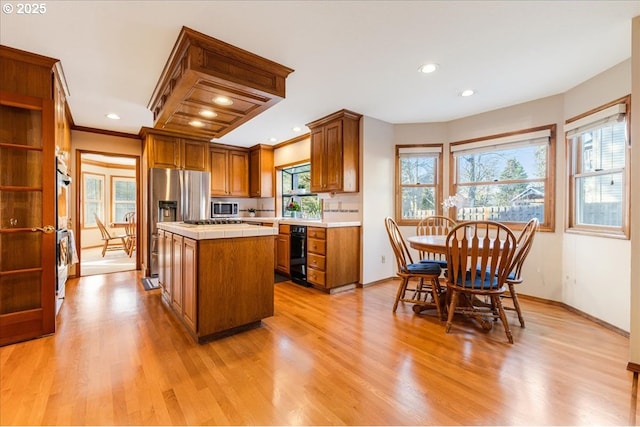 kitchen featuring crown molding, appliances with stainless steel finishes, light hardwood / wood-style floors, a kitchen island, and tile countertops