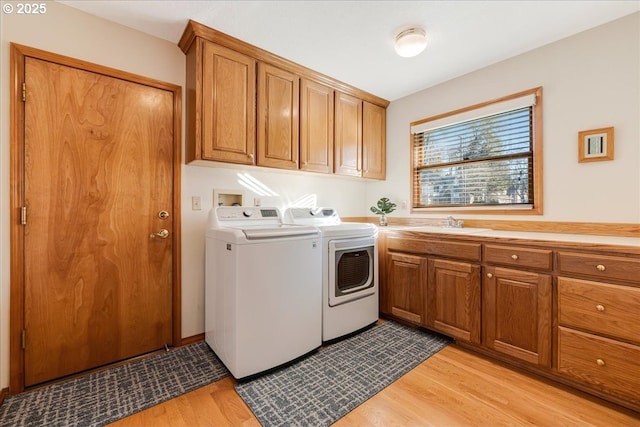 laundry area with washer and dryer, sink, light hardwood / wood-style floors, and cabinets