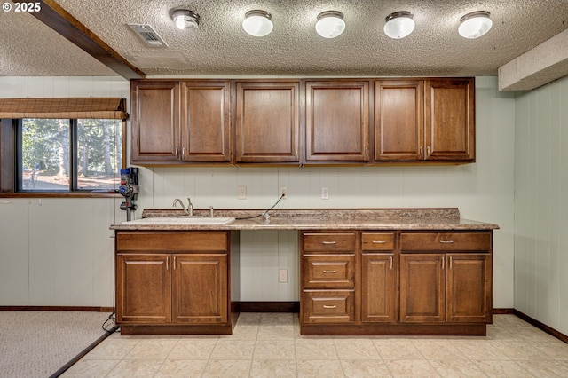 kitchen with brown cabinetry, visible vents, a sink, and a textured ceiling