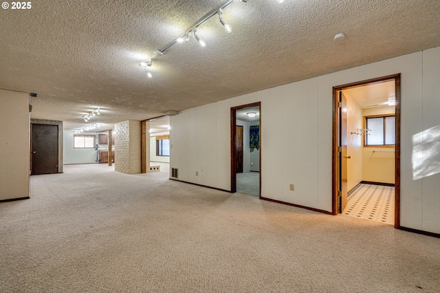 spare room featuring light colored carpet, baseboards, rail lighting, visible vents, and a textured ceiling