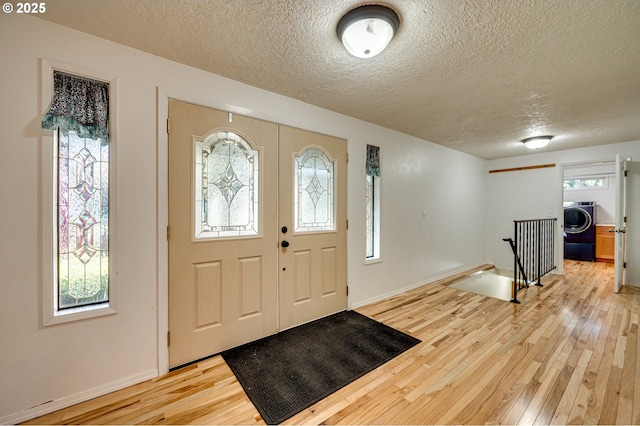 foyer with baseboards, light wood-type flooring, washer / clothes dryer, and a textured ceiling