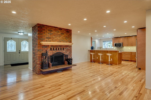 living area featuring light wood-style floors, baseboards, a brick fireplace, a textured ceiling, and recessed lighting