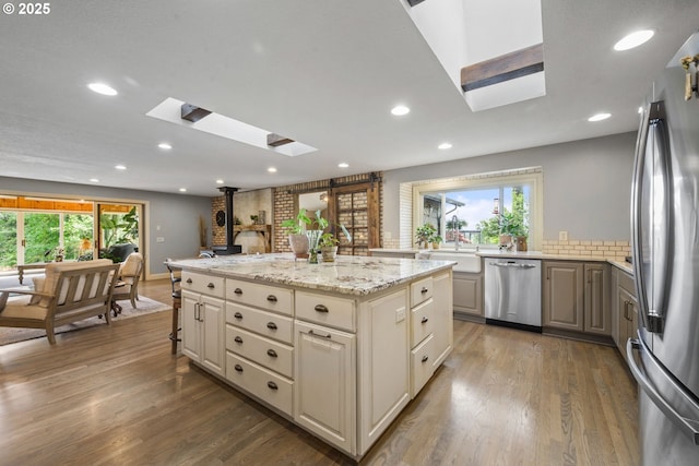 kitchen featuring a skylight, stainless steel appliances, a sink, a center island, and wood finished floors