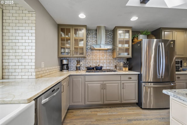 kitchen with stainless steel appliances, wall chimney exhaust hood, light wood-style flooring, decorative backsplash, and light stone countertops