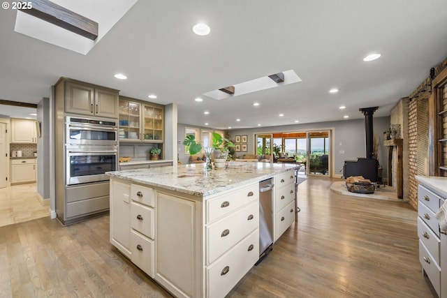 kitchen with a skylight, a wood stove, stainless steel double oven, open floor plan, and light wood-type flooring