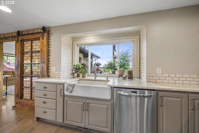 kitchen with stainless steel dishwasher, a sink, gray cabinetry, and backsplash