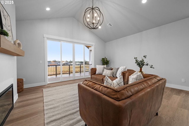 living room featuring light wood-type flooring, a glass covered fireplace, visible vents, and baseboards