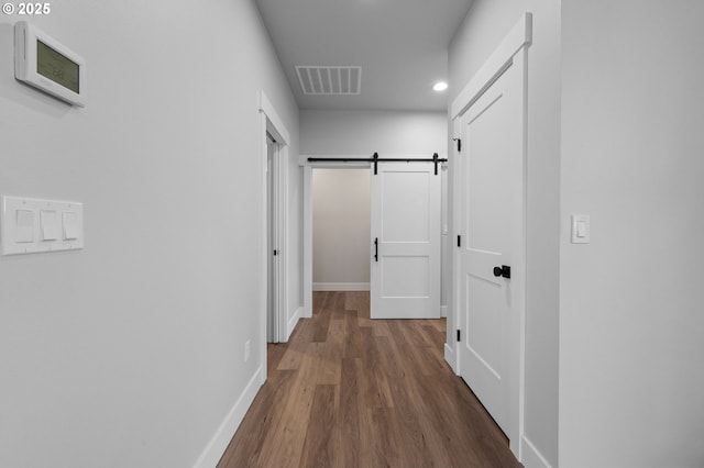 corridor with dark wood-style floors, visible vents, baseboards, and a barn door