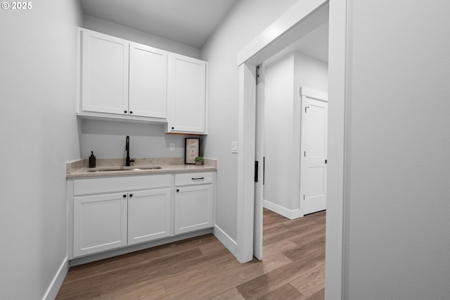 bar with baseboards, a sink, and light wood finished floors